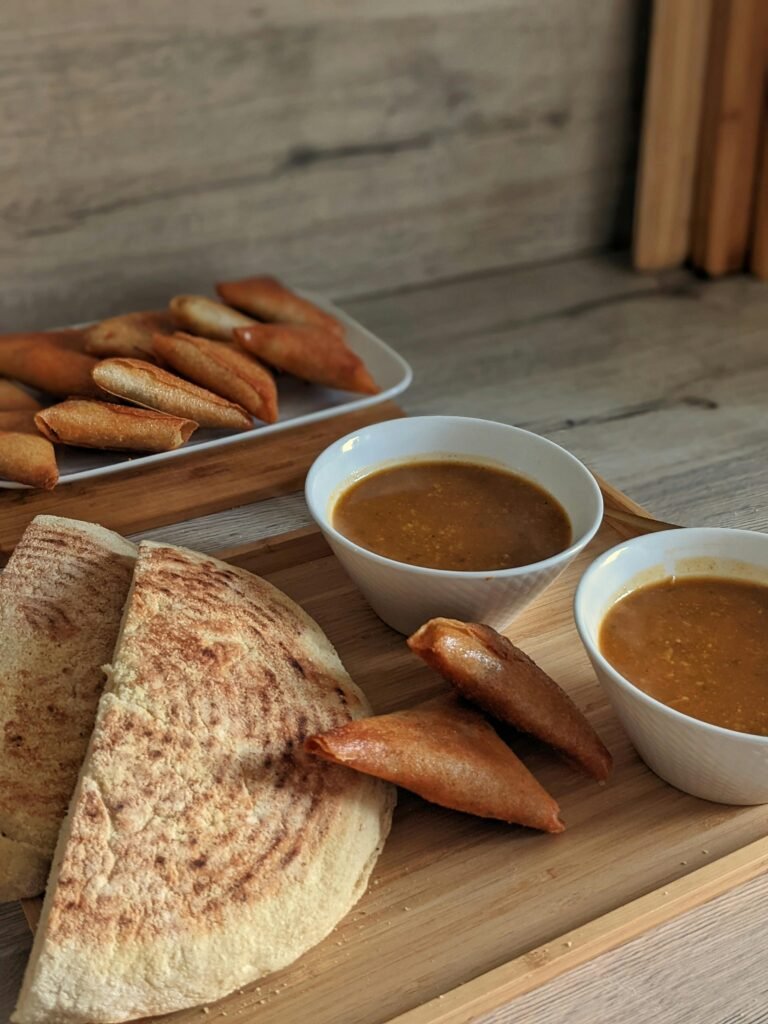 A rustic still life of traditional flatbread, savory samosas, and bowls of rich soup in a cozy setting.