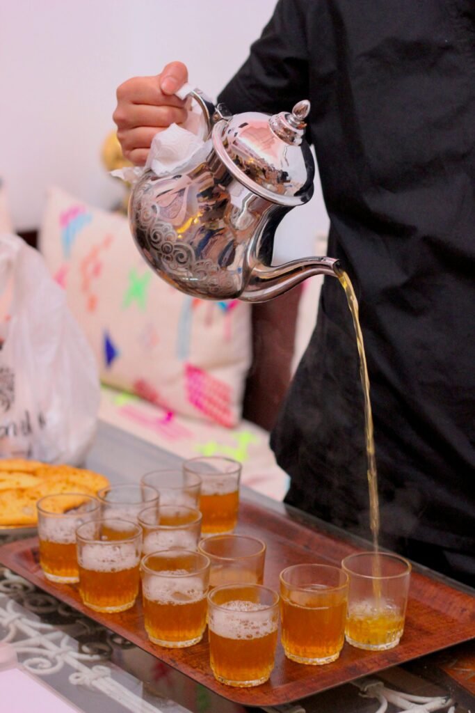 A person elegantly pouring hot tea from a Moroccan teapot into glasses, showcasing cultural tradition.